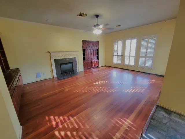 a view of an empty room with wooden floor fireplace and a window