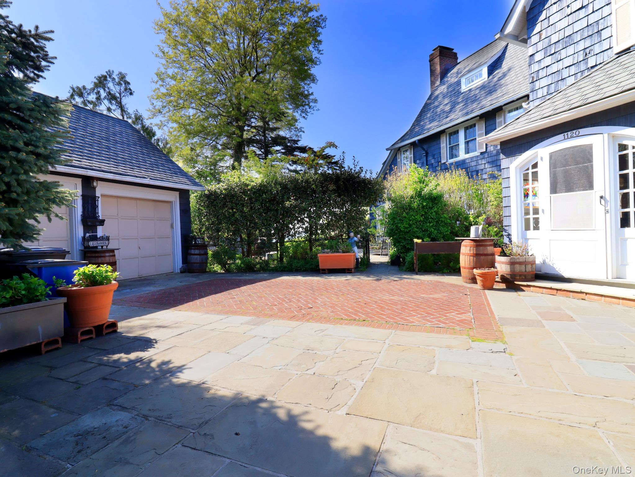 11-20 Shore Road Queens, NY 11363 - Photo 41 of 45 Stone paver patio with a brick inlay, surrounded by mature landscaping.2 car garage