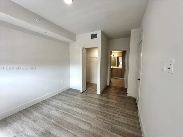 a view of an empty room with wooden floor and a bathroom