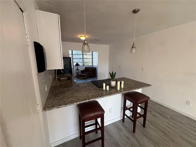 a kitchen with stainless steel appliances granite countertop a sink a refrigerator a stove a dining table and chairs with wooden floor