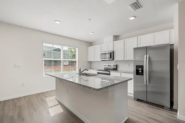 a kitchen with stainless steel appliances granite countertop a sink a stove a refrigerator and white cabinets with wooden floor