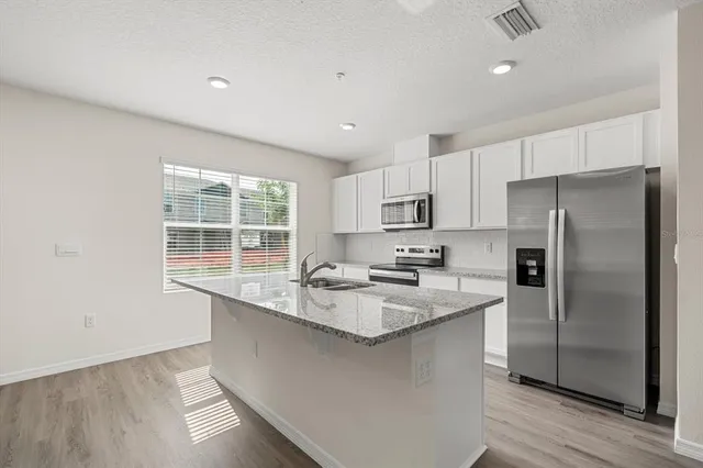 a kitchen with stainless steel appliances granite countertop a sink a stove a refrigerator and white cabinets with wooden floor