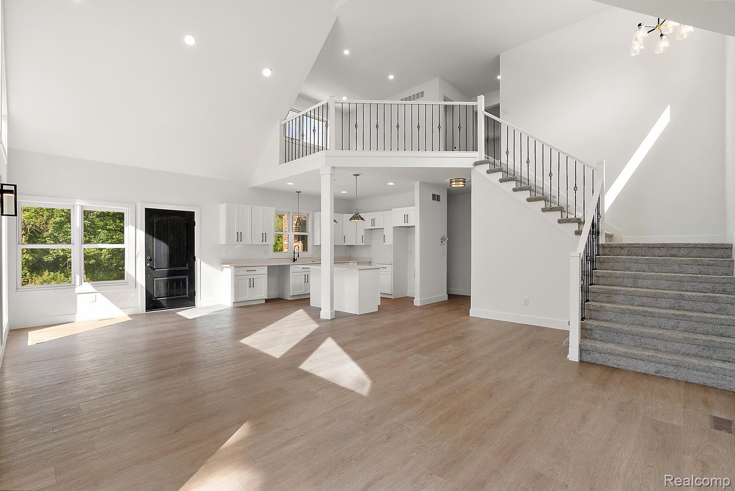 13392 Belsay Road Millington, MI 48746 - Photo 10 of 18 Open-concept layout featuring vaulted ceilings, wood-finish flooring, a contemporary kitchen with white cabinetry, and a carpeted staircase with wrought iron balusters