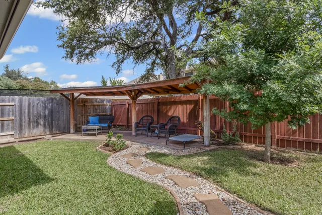 a view of a patio with table and chairs under an umbrella with large trees