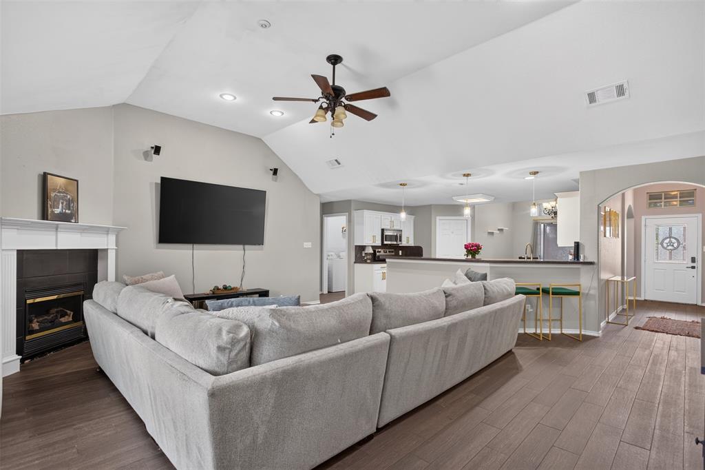 100 Radecke Road Krum, TX 76249 - Photo 12 of 29 Spacious living area featuring wood-finish flooring, a white mantel fireplace, and a vaulted ceiling with a ceiling fan