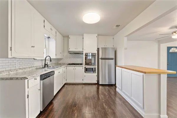 a kitchen with stainless steel appliances granite countertop a refrigerator a sink dishwasher a stove and white countertops with wooden floor