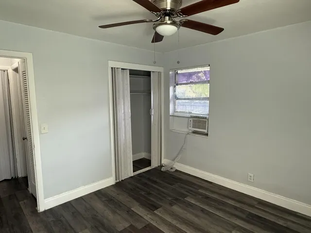 an empty room with wooden floor closet and windows