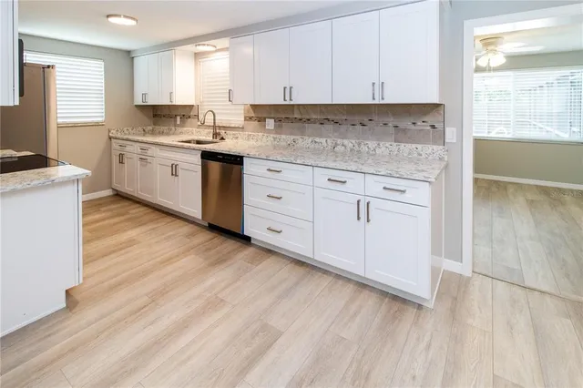 a kitchen with granite countertop white cabinets white appliances a sink and a window