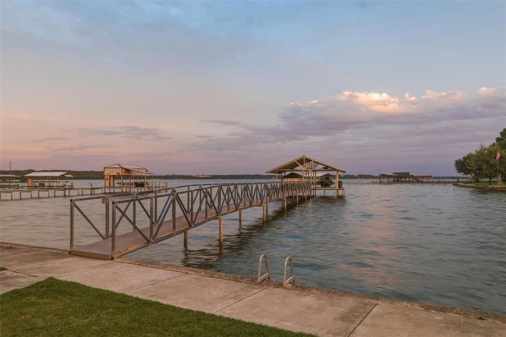 6625 Sandy Beach Road Azle, TX 76020 - Photo 4 of 40 Lake view features open water views across the main body of the lake with private dock access extending from the shoreline. Covered dock structure includes walkway access with metal railing detail and covered boat slip area. Landscaped lawn areas and concrete shoreline edging border the waterfront setting.