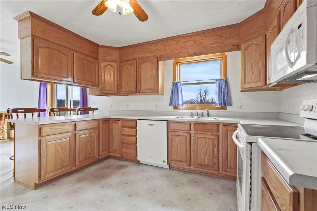 411 Adario West Road Shiloh, OH 44878 - Photo 9 of 35 Kitchen featuring ceiling fan, tasteful backsplash, sink, white appliances, and kitchen peninsula