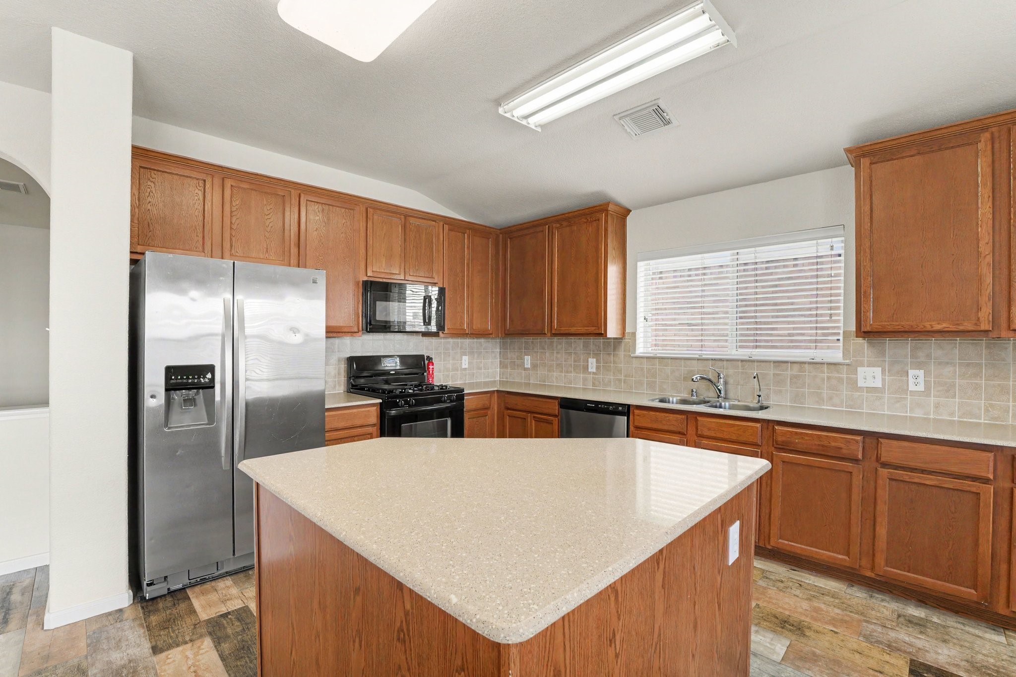 21427 Blooming Rock Lane Spring, TX 77379 - Photo 11 of 32 Spacious kitchen with modern stainless steel appliances, ample wood cabinetry, an island with a solid surface countertop, and a tiled backsplash.