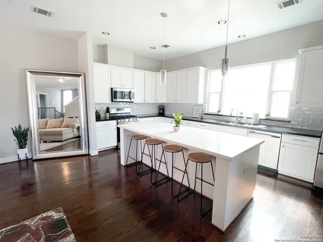 a kitchen with stainless steel appliances granite countertop a stove a sink dishwasher a refrigerator and white cabinets with wooden floor