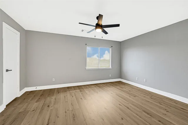 an empty room with wooden floor ceiling fan and windows