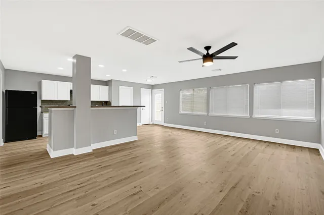 a view of empty room with wooden floor and kitchen view