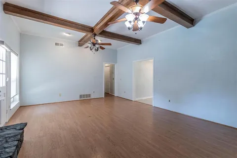 an empty room with wooden floor chandelier fan and windows