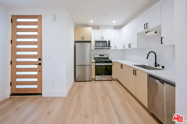 a kitchen with stainless steel appliances a sink dishwasher and a refrigerator with wooden floor