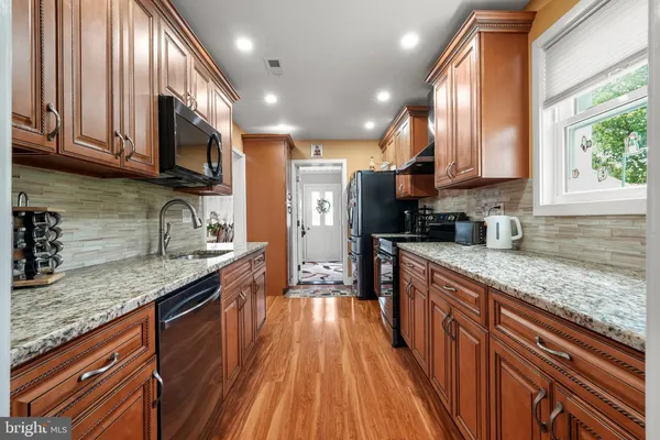 a large kitchen with stainless steel appliances granite countertop a lot of counter space a sink and dishwasher a stove top oven with wooden floor