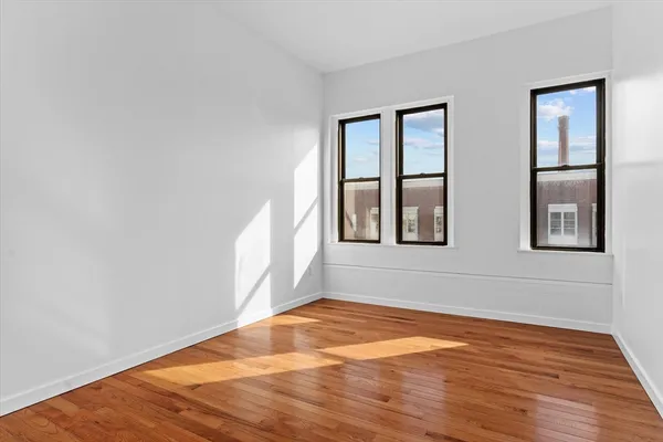 a view of an empty room with wooden floor and windows