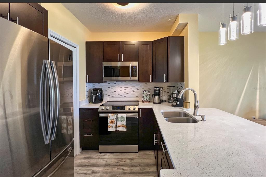 14741 Amberjack Terrace Lakewood Ranch, FL 34202 - Photo 9 of 48 a kitchen with stainless steel appliances granite countertop a refrigerator a stove and a sink with wooden floor
