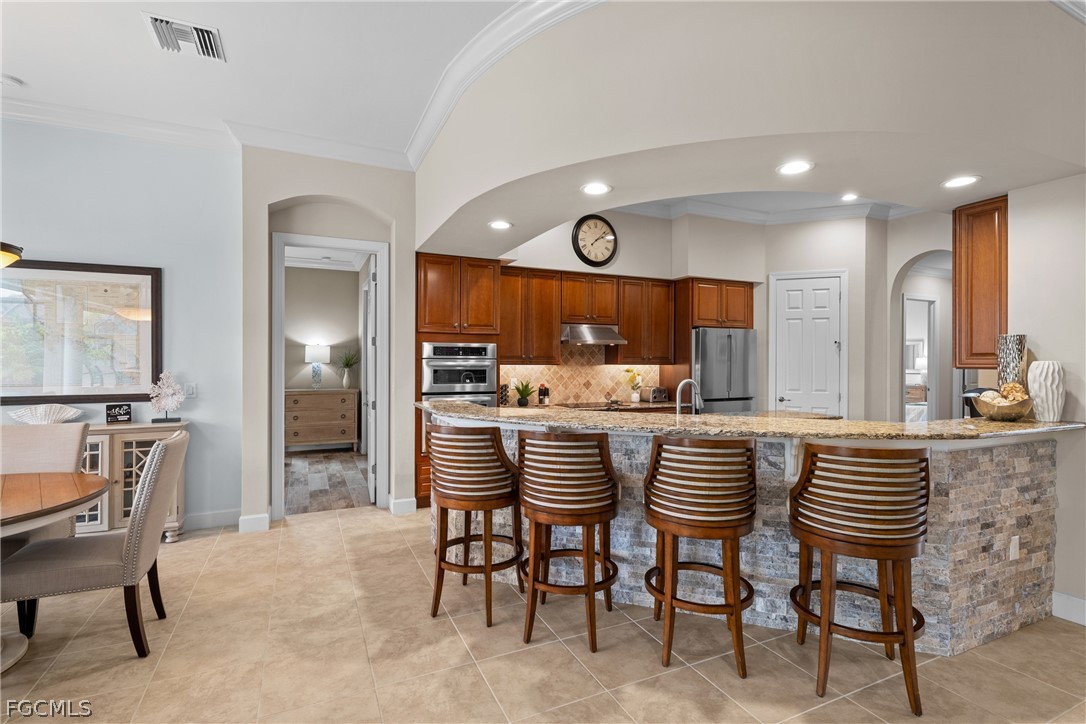 9383 Slate Court Naples, FL 34120 - Photo 10 of 28 a kitchen with stainless steel appliances kitchen island granite countertop a table chairs and a refrigerator