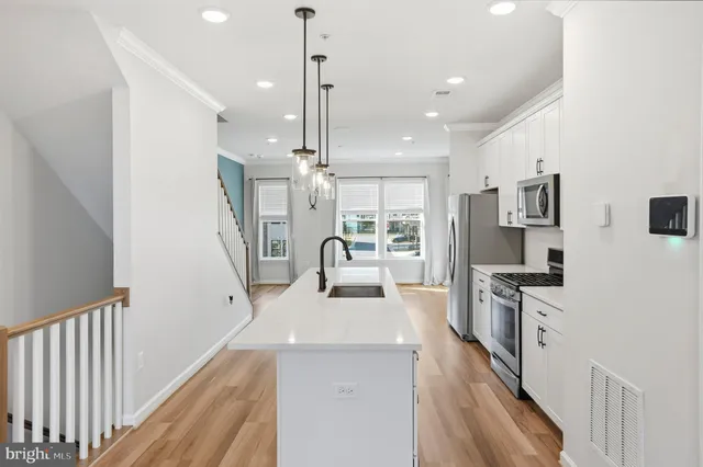 a large white kitchen with stainless steel appliances kitchen island granite countertop a large counter top a stove a chimney a sink and a refrigerator