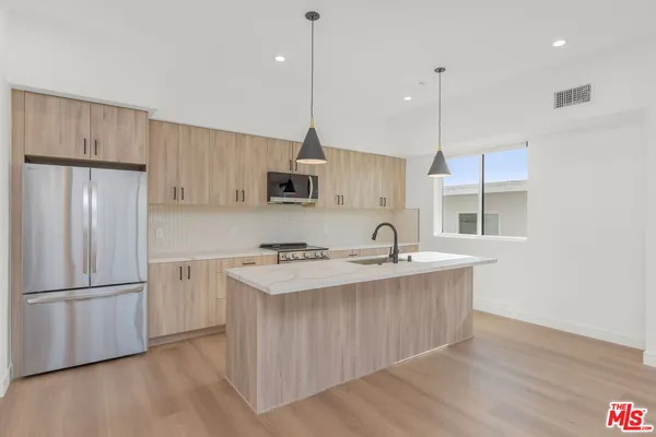 a kitchen with stainless steel appliances granite countertop a sink a stove a refrigerator and island with wooden floor