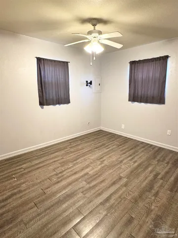 an empty room with wooden floor and way to kitchen
