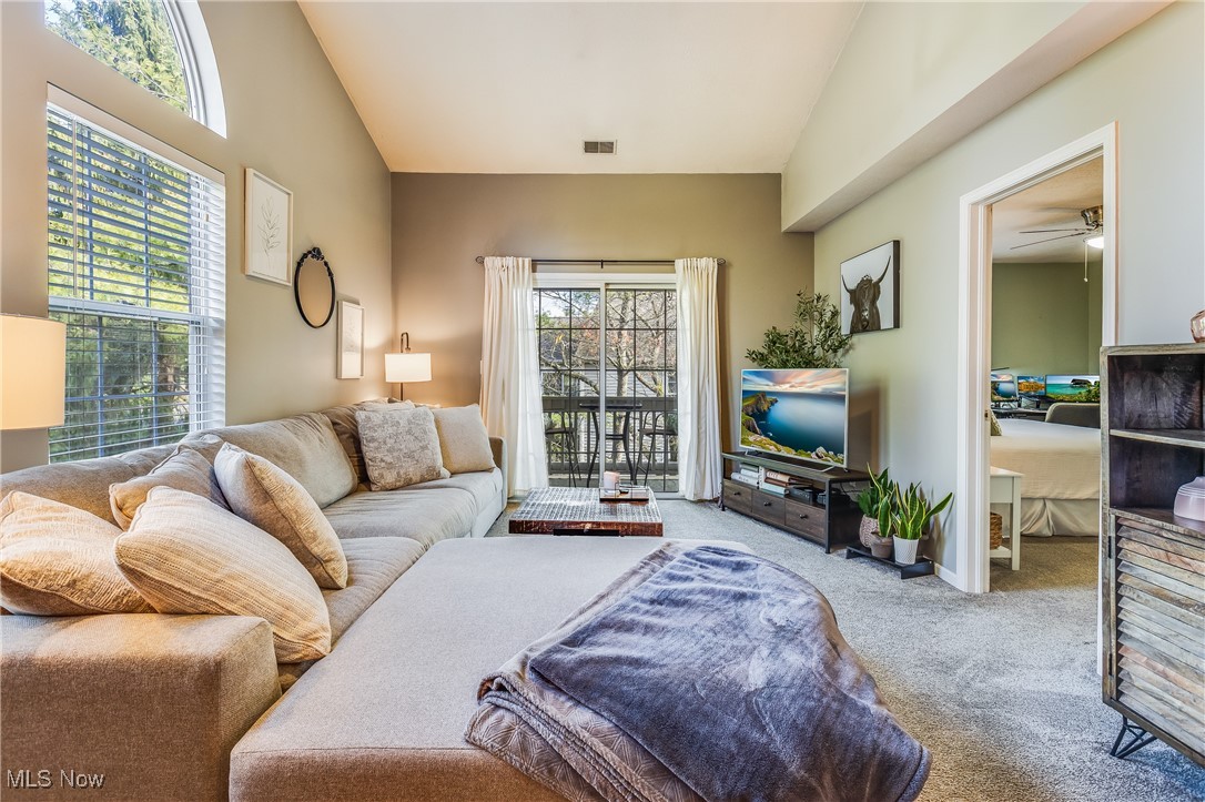 Carpeted living area featuring lofted ceiling, visible vents, and ceiling fan