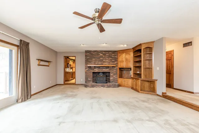 a view of a livingroom with a fireplace a ceiling fan and windows