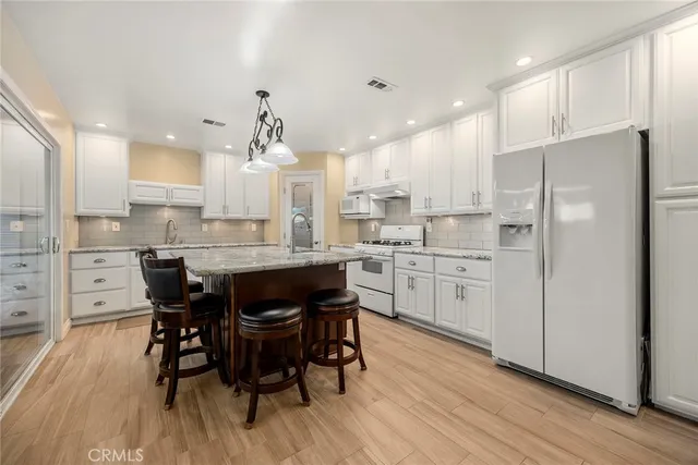 a kitchen with stainless steel appliances kitchen island granite countertop a dining table chairs and white cabinets