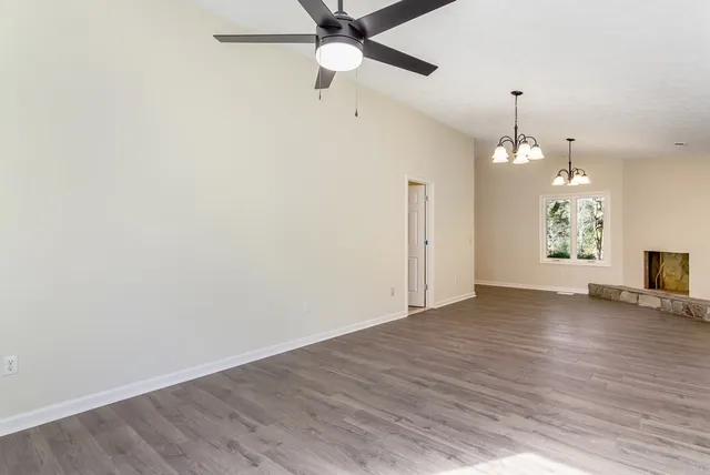 an empty room with wooden floor chandelier fan and windows