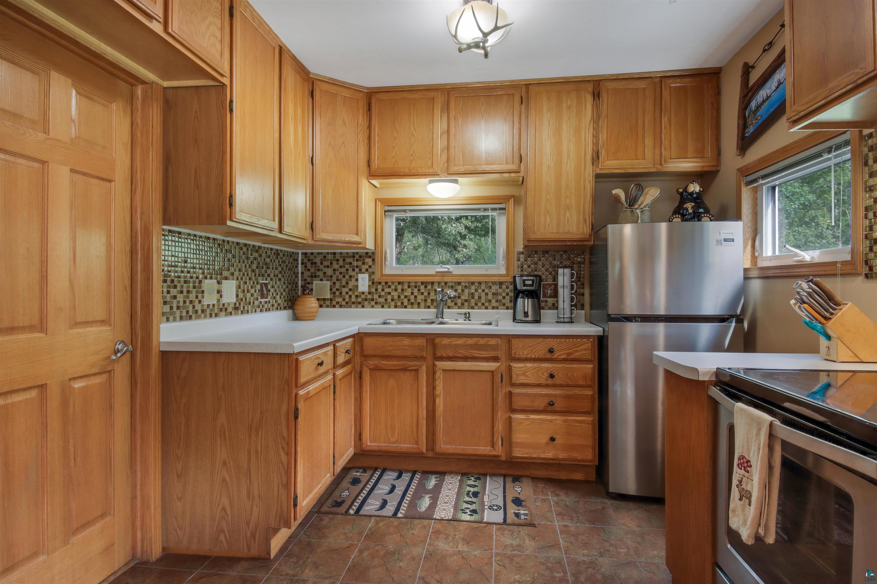 N8348 Island Lake Road Spooner, WI 54801 - Photo 19 of 40 Kitchen featuring sink, decorative backsplash, stainless steel refrigerator, and dark tile patterned flooring