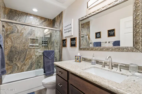 a bathroom with a granite countertop sink a toilet a mirror a vanity and shower