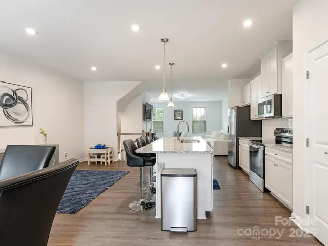 a dining room with stainless steel appliances kitchen island granite countertop a refrigerator a stove a sink and a dining table with wooden floor