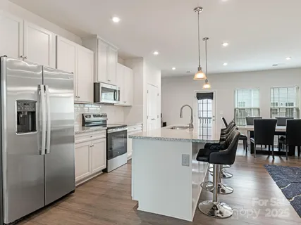 a kitchen with kitchen island granite countertop a refrigerator a stove a sink and white cabinets with wooden floors