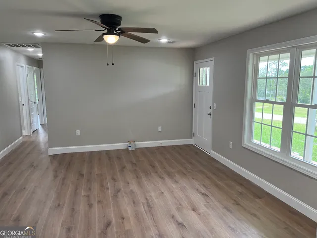 an empty room with wooden floor fan and windows