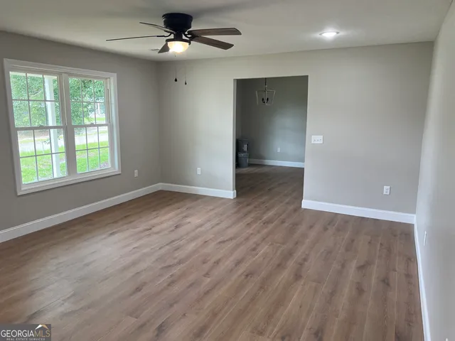 an empty room with wooden floor chandelier fan and windows