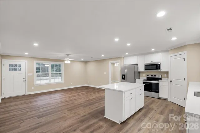 a large kitchen with stainless steel appliances granite countertop a stove top oven a sink a refrigerator and white cabinets with wooden floor