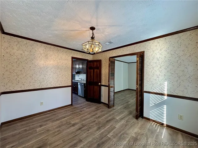 a view of a refrigerator in kitchen and an empty room with wooden floor
