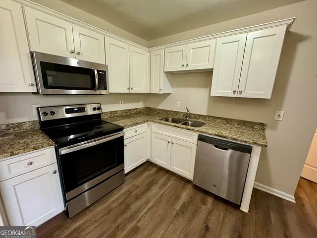 a white kitchen with granite countertop a stove top oven a sink dishwasher and white cabinets with wooden floor