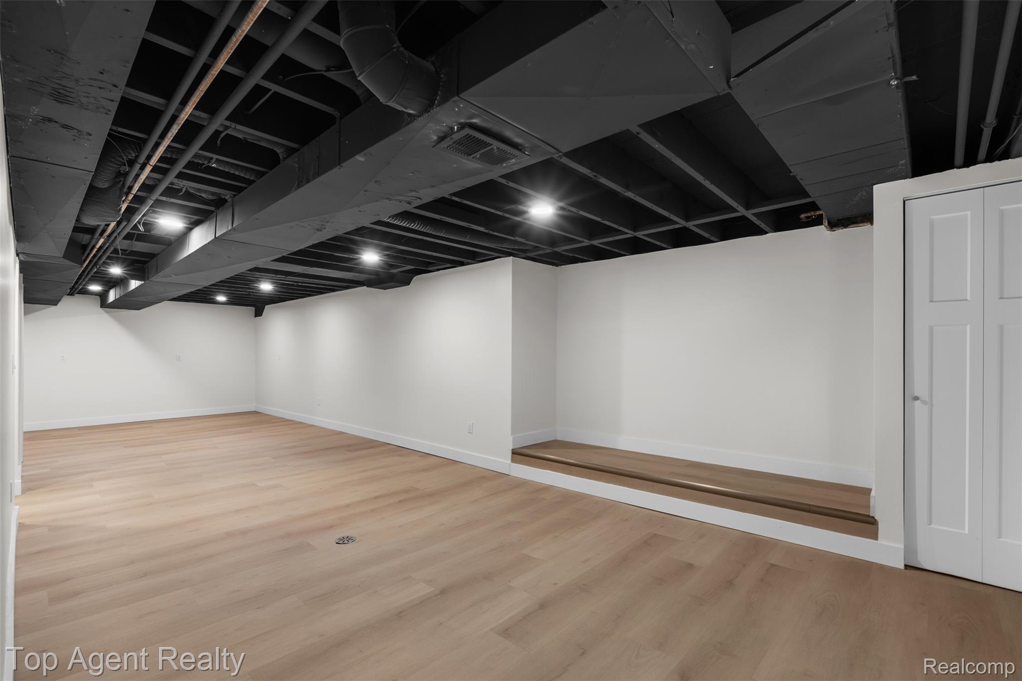 29863 Fall River Road Southfield, MI 48076 - Photo 25 of 50 Spacious room featuring light wood-finish flooring, white walls, and an open black-painted ceiling with recessed lighting
