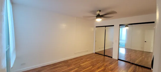 a view of an empty room with wooden floor and a ceiling fan