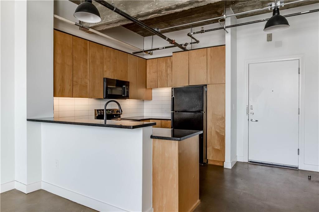 710 Colorado Street, Unit G9 Austin, TX 78701 - Photo 12 of 25 Industrial chic kitchen boasts exposed ductwork, dark countertops, and ample cabinetry for modern living.