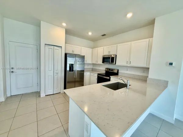 a kitchen with granite countertop a refrigerator a sink and white cabinets