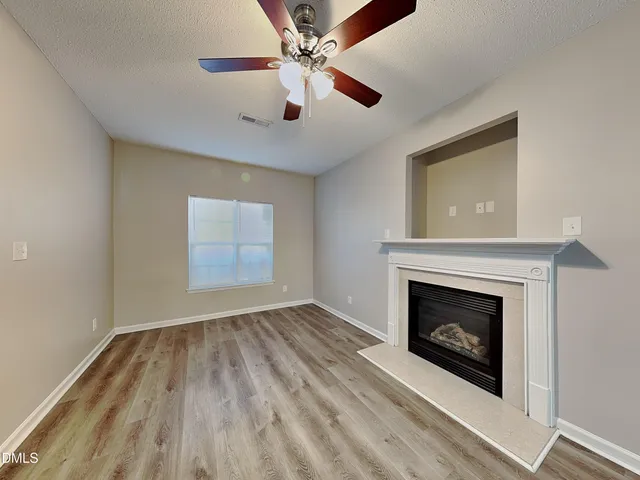 an empty room with windows a fireplace a ceiling fan and wooden floor