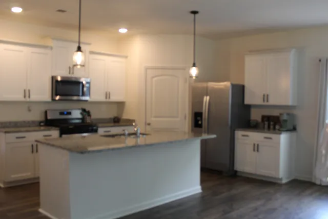 a kitchen with stainless steel appliances granite countertop a sink a stove a refrigerator a center island with wooden floor and cabinets