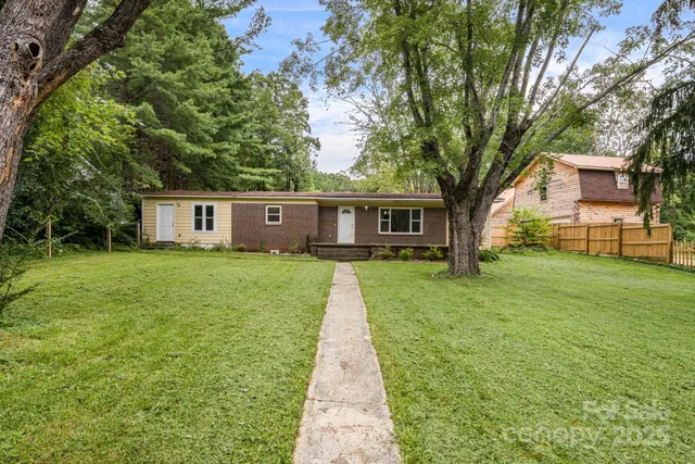 a view of a house next to a big yard and large trees