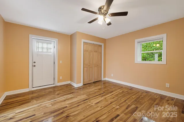 a view of an empty room with wooden floor and a ceiling fan