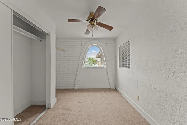 an empty room with a chandelier fan and kitchen view