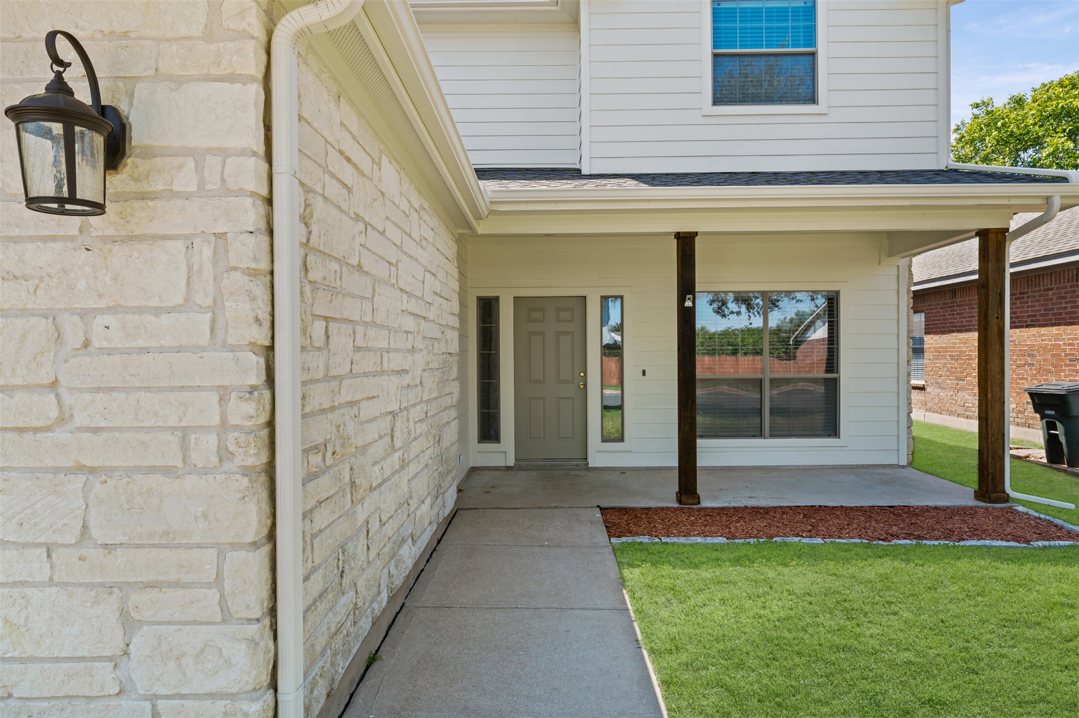 243 Engineers Pass Jarrell, TX 76537 - Photo 3 of 40 Stone facade with sconce lighting, concrete walkway, covered front porch, wood columns, and manicured lawn